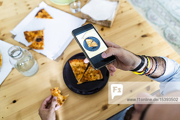 Person  die ein Smartphone-Foto von einem Stück Pizza auf einem Teller macht