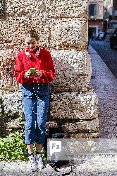 Junge Frau mit rotem Pullover und Smartphone in Verona