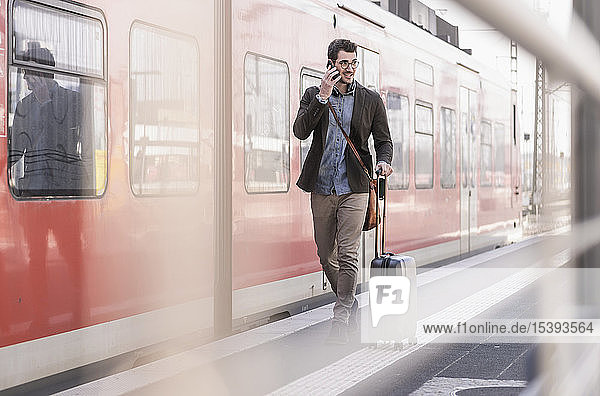 Lächelnder junger Mann mit Handy auf Bahnsteig entlang des S-Bahnsteigs