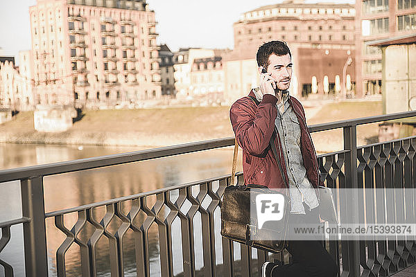 Young man with tablet talking on cell phone on a bridge in the city