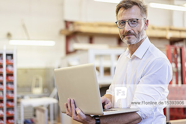 Porträt eines selbstbewussten Geschäftsmannes mit Laptop in der Fabrik