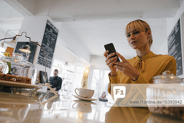Blonde Geschäftsfrau benutzt Smartphone in einem Café und liest Textnachrichten