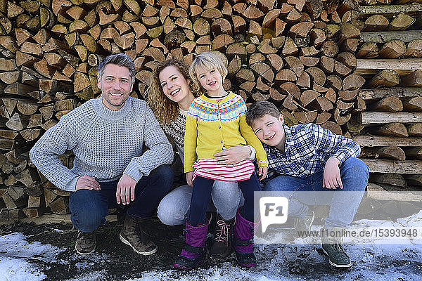 Porträt einer glücklichen Familie vor einem Holzstapel im Winter
