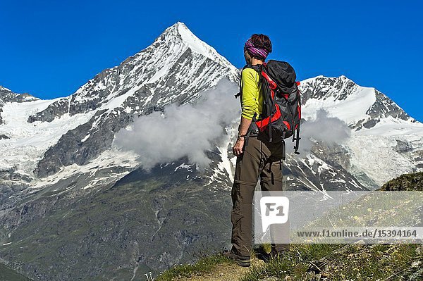 Woman with backpack looking at the Weisshorn peak above the Mattertal valley Täschalp Valais Switzerland.