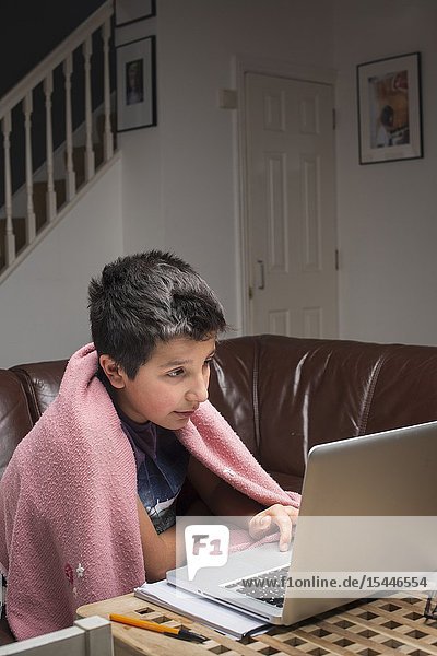 London UK. Boy 10 years old studies in his computer in a cold room.