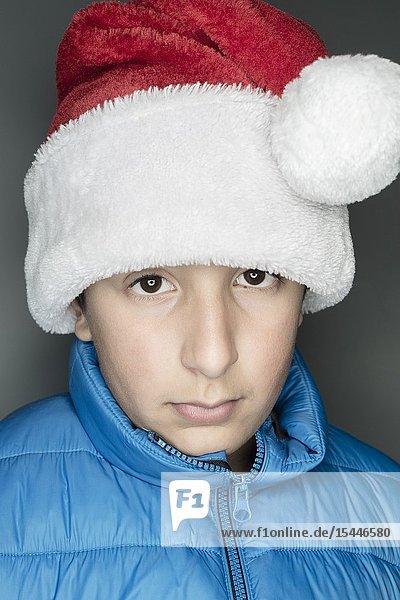11 years old Caucasian boy in bblue jacket and Santa's hat.