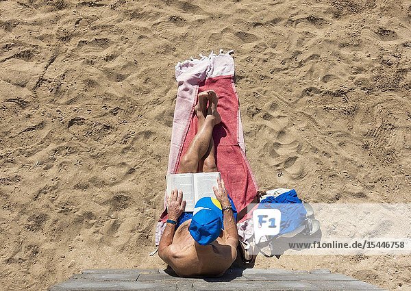 Elderly man reading book on Las Canteras beach in Las Palmas Gran Canaria Canary Islands Spain.