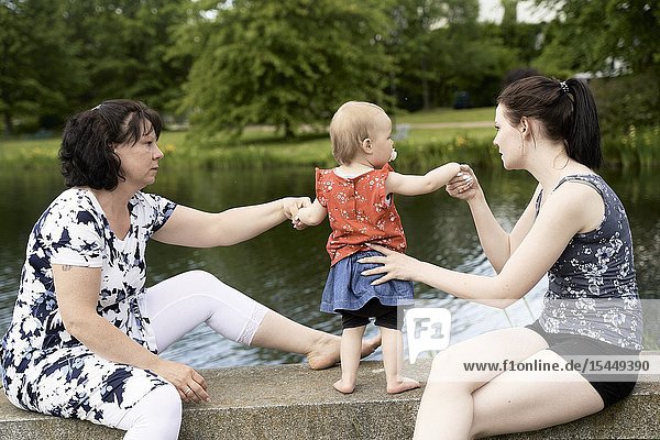 Caring mother and grandmother holding baby toddler child on hands security outdoors next to lake in park
