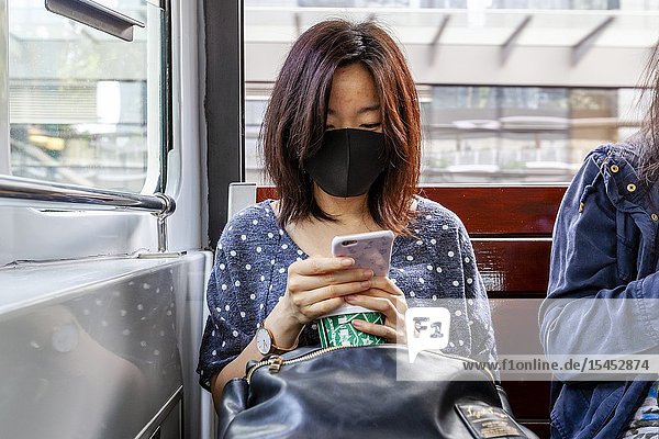 A Woman Wearing A Face Mask Sitting On A Tram Looking At Her Smartphone Hong Kong China.