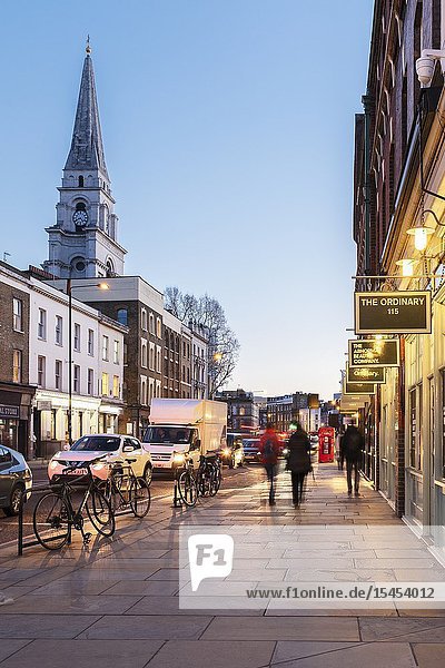 Brushfield Street with designer shops on the South side of Spitalfieds Market and Christ Church Spitalfieds at night London UK.