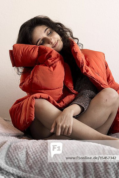 Young emotive woman sitting on bed with red winter jacket