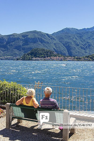 Tourists look at Bellagio from a bench on the shore of Lake Como Lombardy Italy.