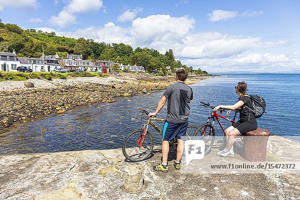 Two cyclists standing on the harbour at the small village of Sannox and looking at the view Sannox Isle of Arran on the Firth of Clyde Scotland.