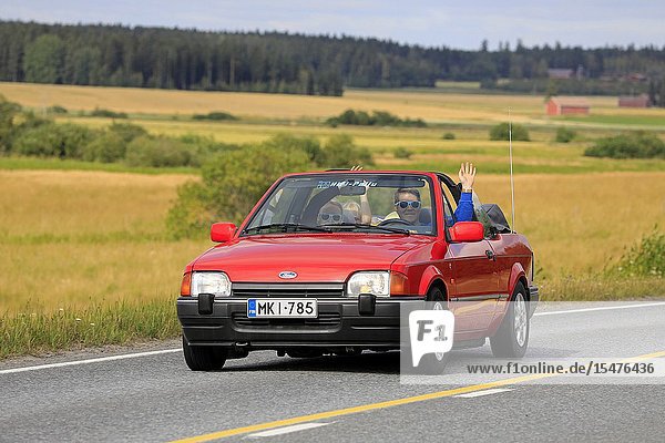 Vaulammi Finland. August 3 2019. Family smiling and waving on 1990s red Ford Escort cabriolet on Maisemaruise 2019 car cruise. Credit: Taina Sohlman