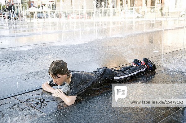 Tilburg Netherlands. Teenage boy playing with fountain water during the hot summer and the annual carnival and fair.