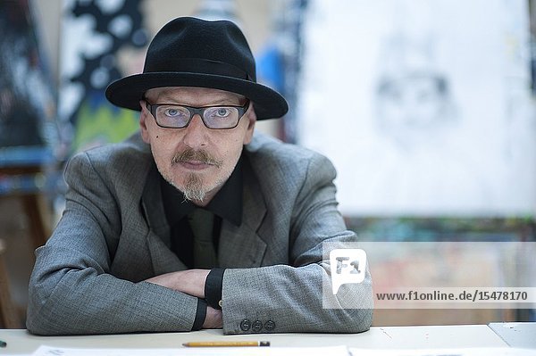 Rotterdam Netherlands. Senior adult male wearing a hat sitting at the Via Kunst atelier and art shop table while working on a new drawing.
