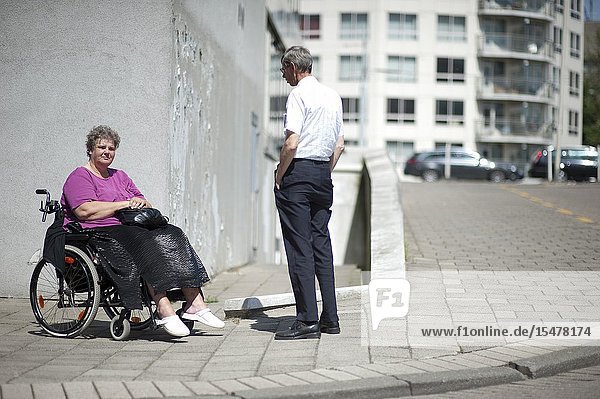 Rotterdam Netherlands. Woman in Wheel chair talking to a walking neighbor on the sidewalk of her neighborhood residential street.