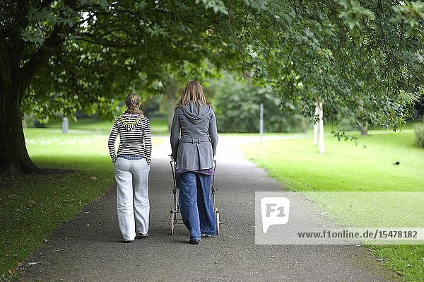 Rotterdam Netherlands. A new mother with her baby in a carriage walking and strolling Kralingen Forrest (Kralingse Bos) with a female friend while they are having a conversation.