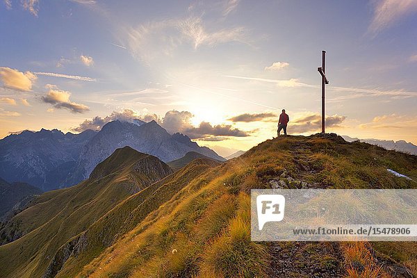 A hiker admires the sunset on Marmolada group from the grassy summit of Migogn Mount Dolomites Marmolada group Rocca Pietore Belluno province Veneto Italy.