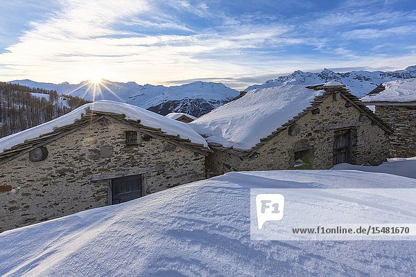 Sunburst on the snowy huts Alpe Groppera Madesimo Valchiavenna Valtellina Sondrio province Lombardy Italy.
