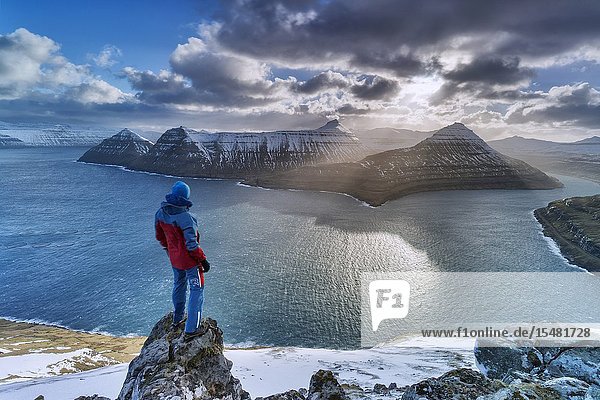 Hiker on rocks admiring the rays of sun over Funningur fjord Eysturoy island Faroe Islands Denmark.