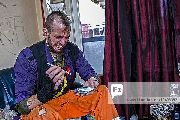 Rotterdam Netherlands. Worn out caucasian male using hard drugs and speed while sitting on his chaotic living room coach. His tae of drug abuse is fuel by the wish to self medicate and keep his head into silence.