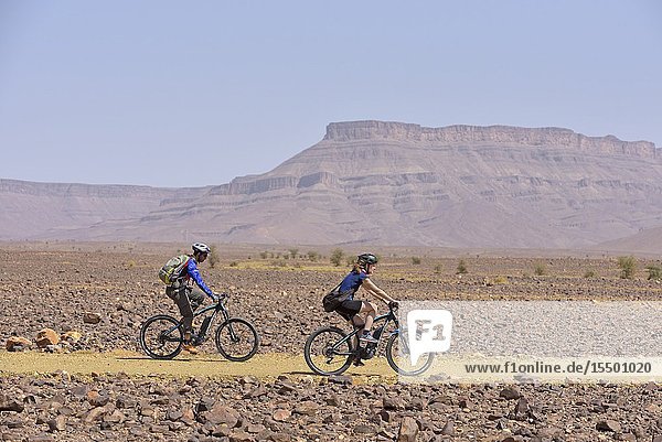 Mountain bikers with electric assistance on a trail through the reg from Agdz to Zagora Draa River valley Province of Zagora Region Draa-Tafilalet Morocco North West Africa.