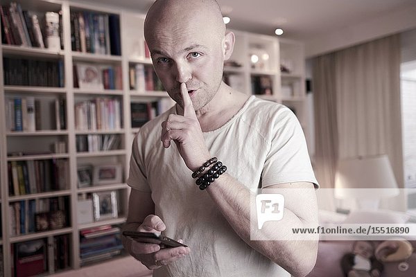 Man with phone and finger on lips looking at camera