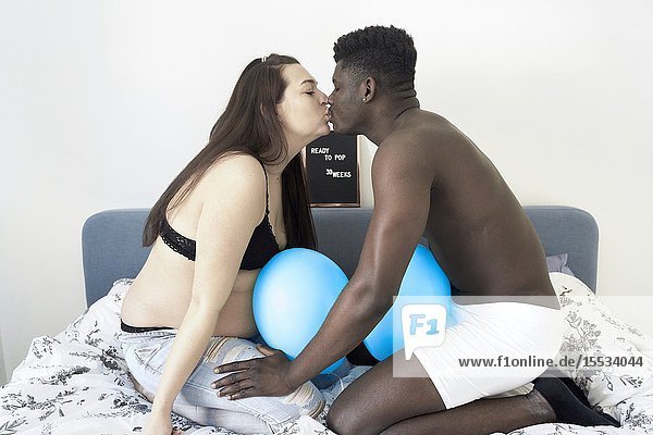 Pregnant woman kissing African man in bed