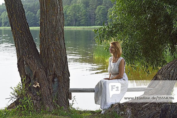 Woman sitting on a bench on the edge of Lusiai Lake at Paluse Aukstaitija National Park Lithuania Europe.