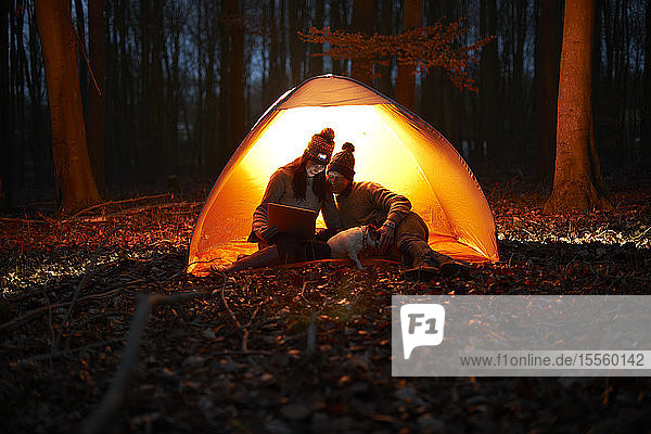 Paar benutzt digitales Tablet im leuchtenden Zelt im nächtlichen Wald