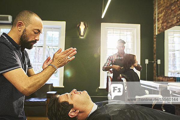 Male barber standing over customer in barbershop