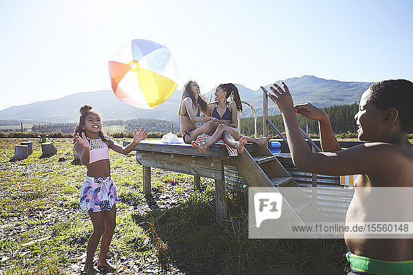 Verspieltes lesbisches Paar und Kinder mit Strandball an einem abgelegenen  sonnigen Sommerpool