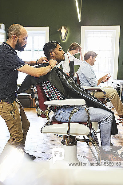 Männlicher Friseur  der einen Kunden auf einen Haarschnitt vorbereitet  in einem Friseursalon