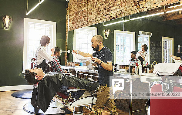 Male barber preparing to steam face of customer before shave in barbershop