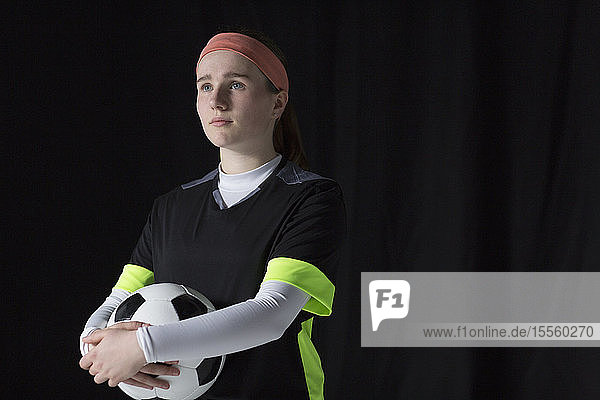 Porträt einer selbstbewussten  ehrgeizigen Fußballspielerin im Teenageralter  die einen Ball hält