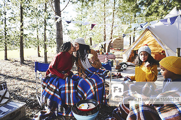Zärtliches lesbisches Paar mit Kindern küsst sich auf einem sonnigen Campingplatz im Wald