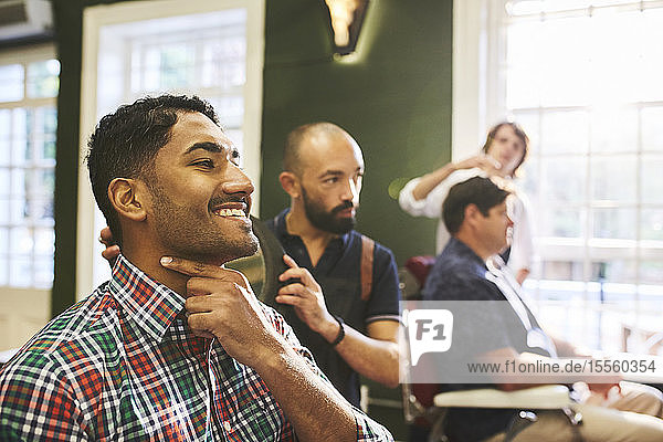 Lächelnder männlicher Kunde  der sein rasiertes Gesicht im Friseursalon überprüft