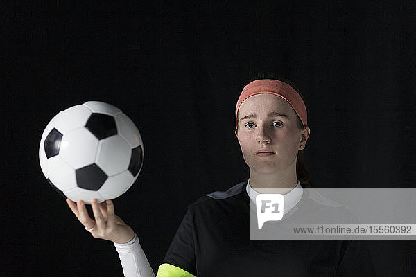 Porträt einer selbstbewussten  entschlossenen Fußballspielerin im Teenageralter  die einen Fußball hält