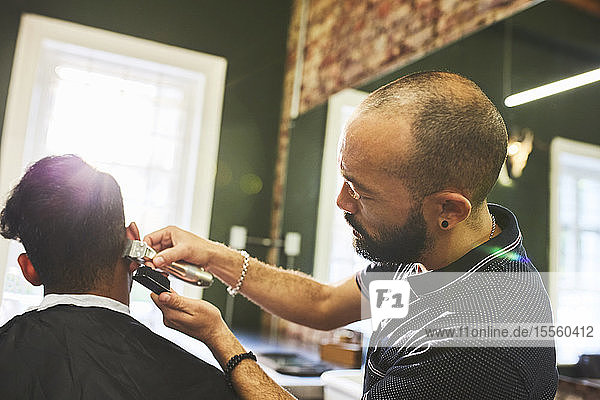 Male barber with trimmers giving customer haircut in barbershop