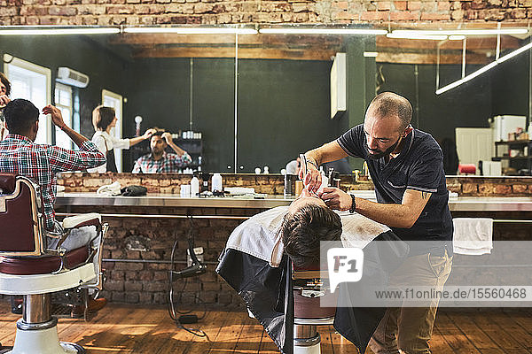 Male barber shaving face of customer in barbershop