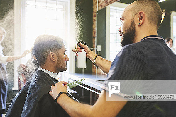 Männlicher Friseur sprüht die Haare eines Mannes im Friseursalon