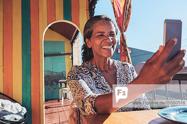 Lächelnde  glückliche Frau  die ein Selfie mit ihrem Smartphone auf einer sonnigen Terrasse macht