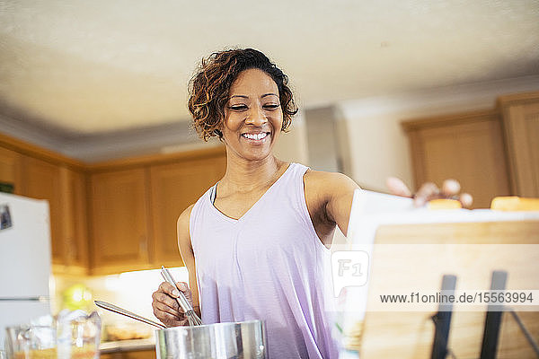 Smiling woman with cookbook cooking in kitchen
