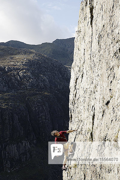 Männlicher Bergsteiger  der eine große Felswand erklimmt und nach oben schaut