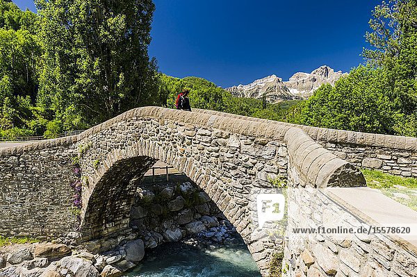 Young hiker crossing the old bridge of Bolática River Panticosa Tena Valley Pyrenees (Huesca province Aragón Spain)