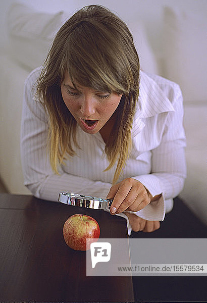 Frau betrachtet Apfel durch eine Lupe