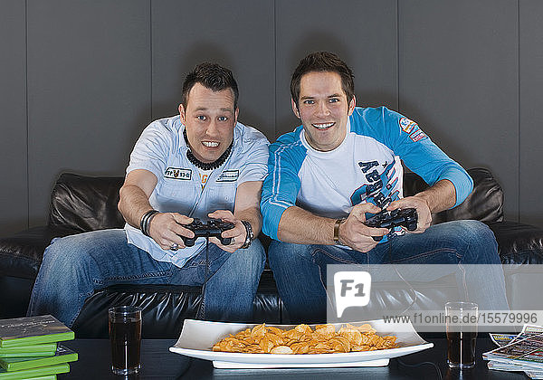 Männer sitzen lächelnd auf der Couch und spielen Videospiele