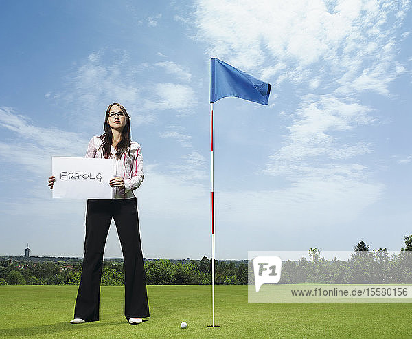 Deutschland  Junge Frau mit Plakat auf dem Golfplatz