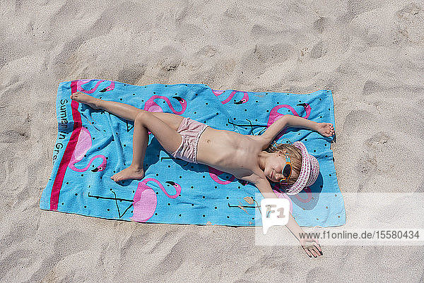 Top view of little girl lying on beach towel on the beach